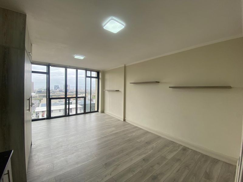 A bright, empty bedroom featuring modern laminate flooring, built-in storage, floating shelves, and large windows offering an expansive city view.