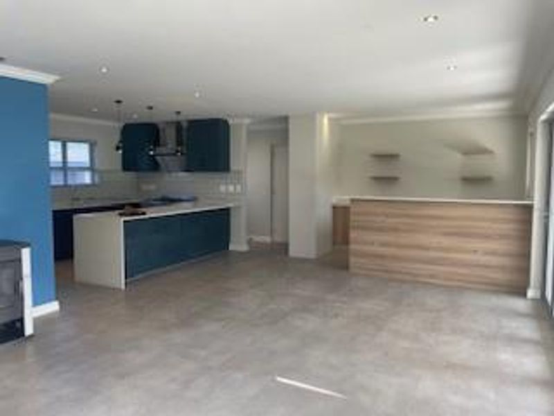 Spacious open-plan living area featuring a modern kitchen with a central island, breakfast bar, and sleek cabinetry, complemented by neutral tiled flooring.