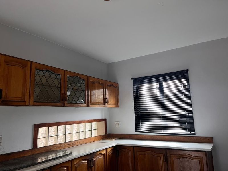 A functional kitchen area featuring traditional wooden cabinetry, laminate countertops, and a unique glass block backsplash, offering a classic aesthetic ready for modernization.