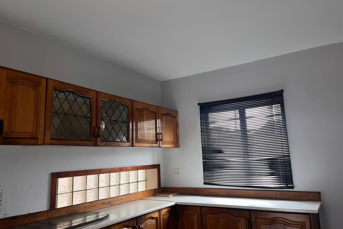 A functional kitchen area featuring traditional wooden cabinetry, laminate countertops, and a unique glass block backsplash, offering a classic aesthetic ready for modernization.