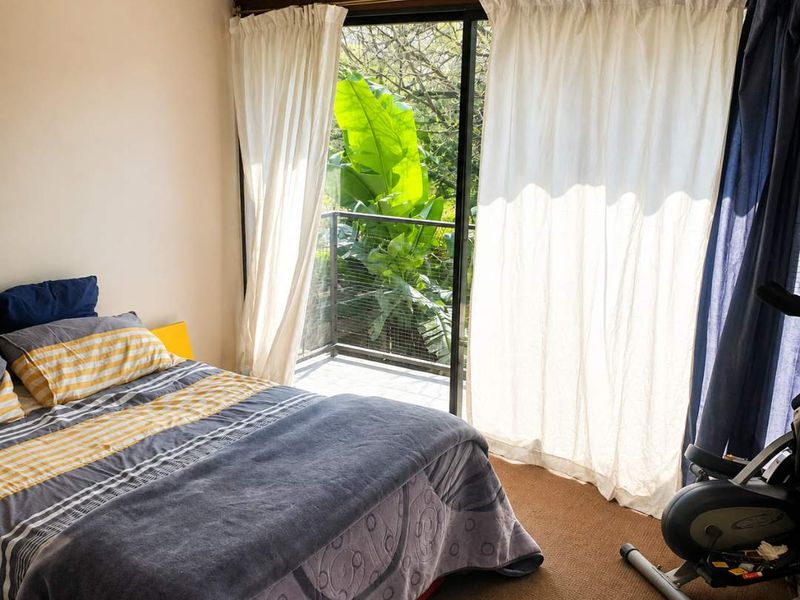A bedroom featuring a ceiling fan and large sliding glass doors that open onto a private balcony with lush greenery views.