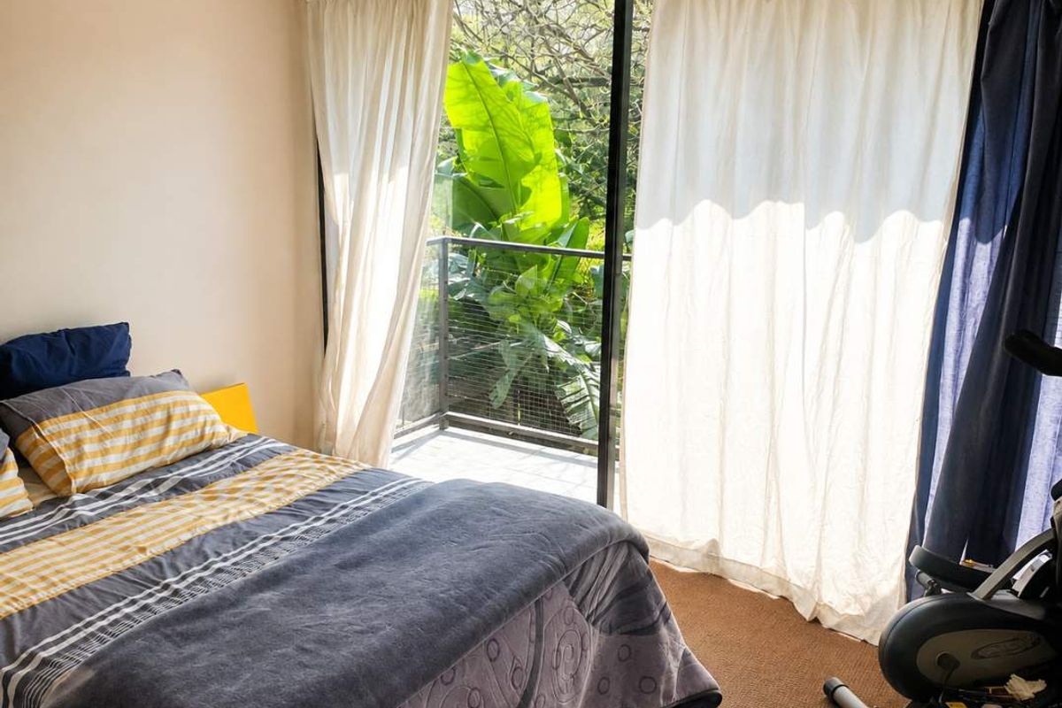 A bedroom featuring a ceiling fan and large sliding glass doors that open onto a private balcony with lush greenery views.
