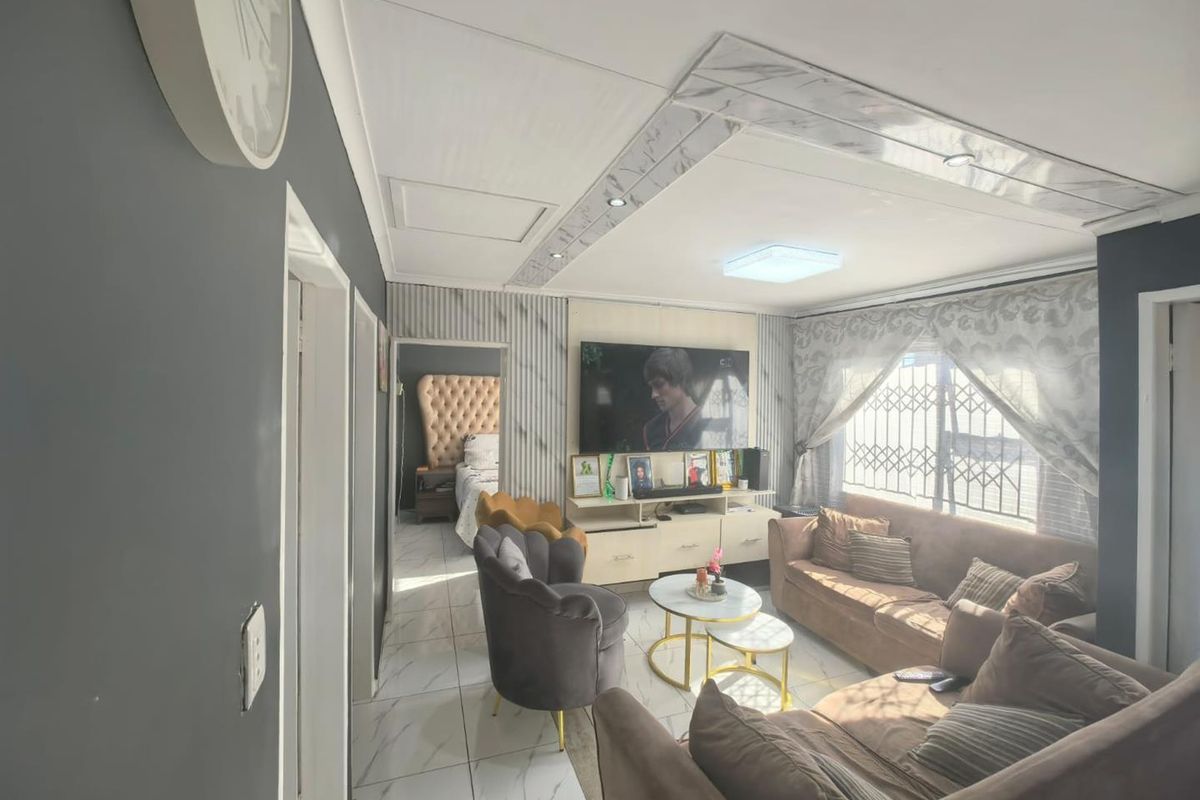 A living room featuring tiled flooring, a decorative recessed ceiling detail with integrated lighting, and security bars on the windows.