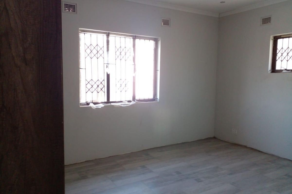A clean, empty bedroom featuring light-toned tiled flooring, neutral walls, and security bars on the windows.