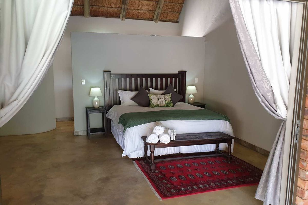 Spacious bedroom featuring a high thatched roof, polished concrete flooring, and a neutral color palette, offering a comfortable and rustic atmosphere.