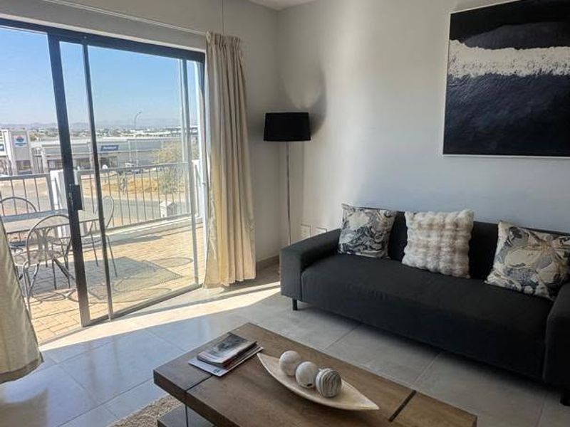 A bright living room featuring tiled flooring and a large sliding glass door that opens onto a balcony with outdoor views.