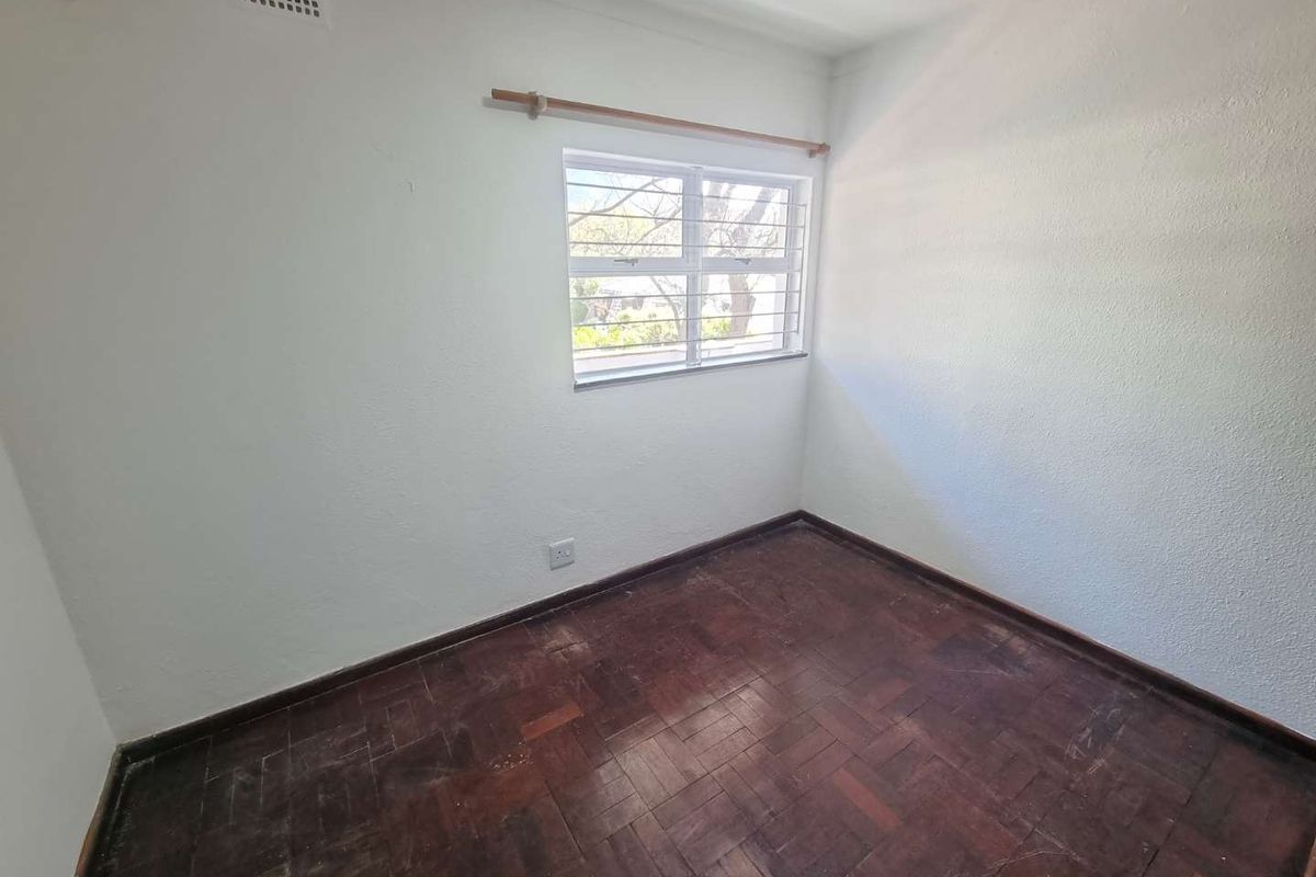An empty bedroom featuring original parquet flooring, a window with security bars, and a neutral wall finish, ready for renovation or staging.