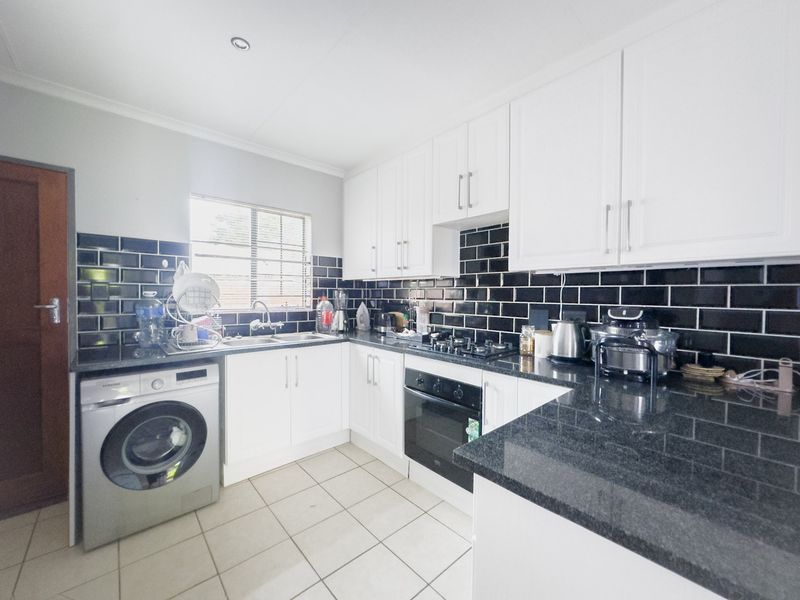 A functional kitchen featuring white cabinetry, granite countertops, a black subway tile backsplash, and integrated appliances including an oven and gas hob.