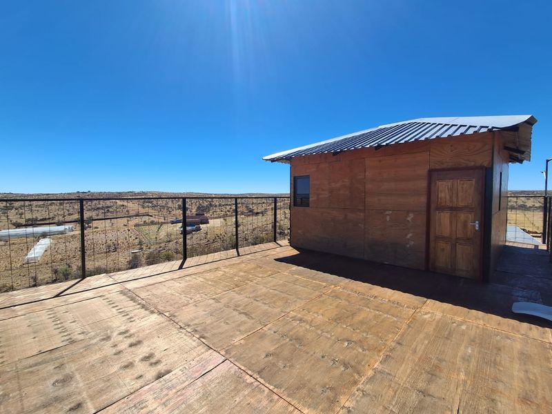 Elevated outdoor deck area featuring plywood flooring, wire mesh balustrade, and a small timber structure with a corrugated metal roof, overlooking the surrounding landscape.