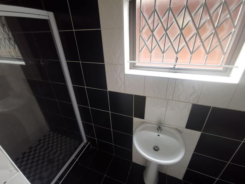 A clean bathroom featuring a pedestal basin, shower enclosure, and high-contrast black and white wall tiling with a window security gate.