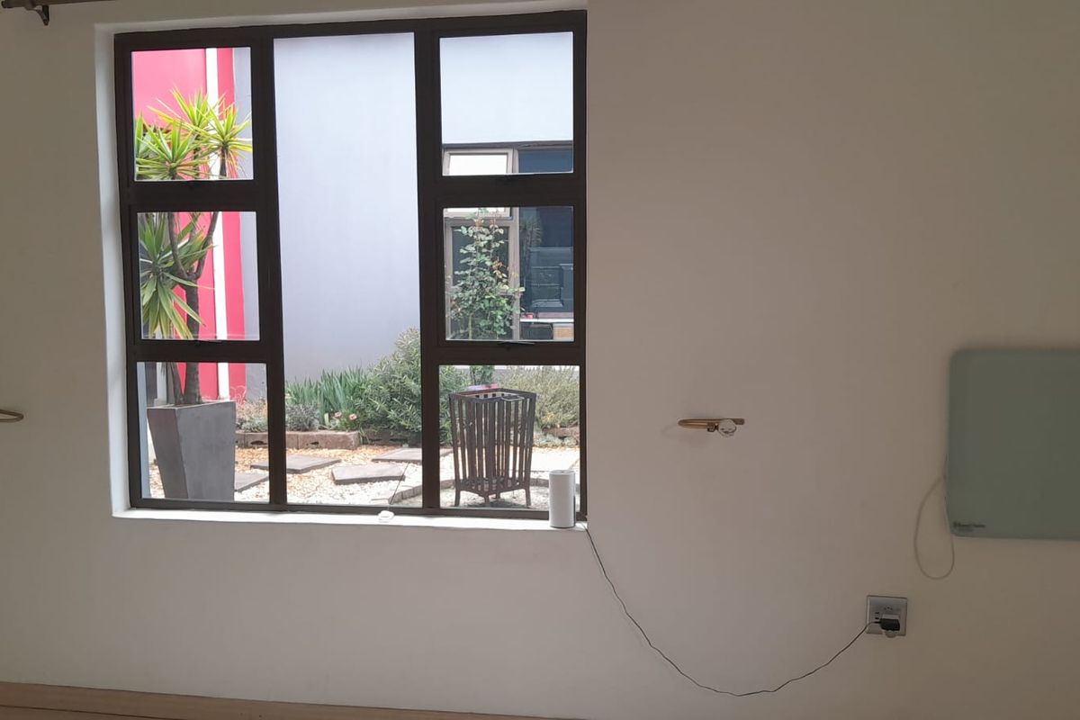 An empty living room featuring a large aluminium-framed window with a view of the garden and a wall-mounted heater.