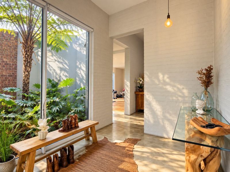 A bright, modern hallway featuring polished concrete floors, painted brick walls, and a large glass door overlooking a lush private courtyard.