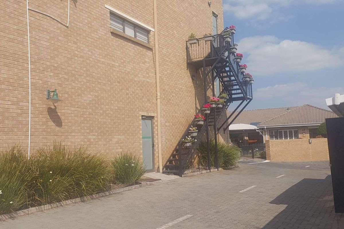 Rear exterior view of the retirement village building featuring a brick facade, paved driveway, and an external metal staircase providing access to upper levels.