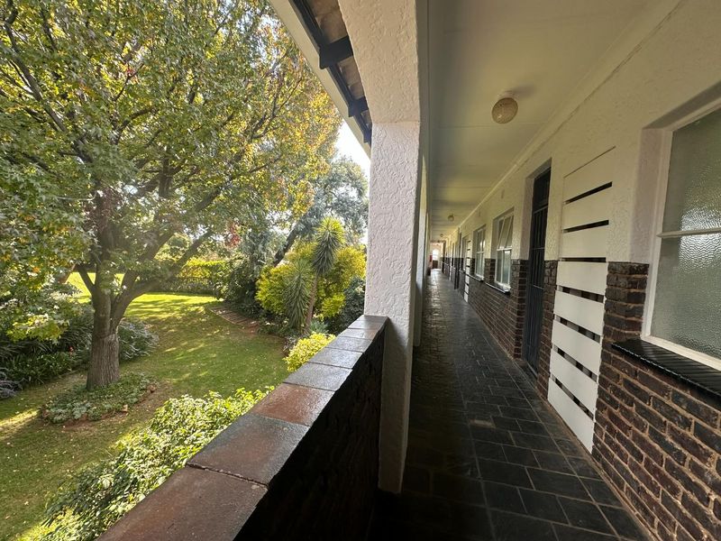 A long, covered exterior walkway or balcony featuring tiled flooring, brick accents, and views overlooking a landscaped garden area.