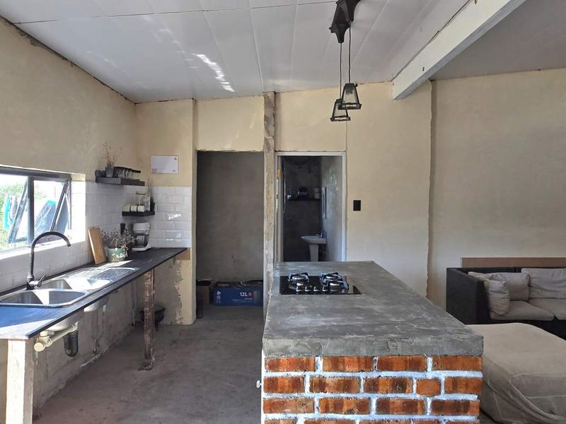Open-plan living and kitchen area featuring a brick-based island with concrete countertop, gas hob, and subway tile backsplash, currently in an unfinished state.