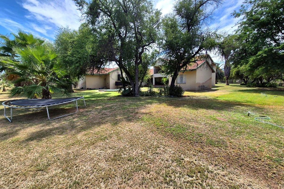 A view of the rear exterior of the farm property, featuring a spacious garden with mature trees and a large lawn area.