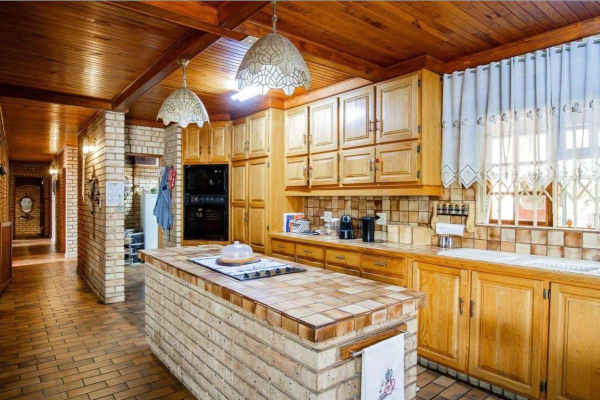 Spacious kitchen featuring timber cabinetry, a brick island with integrated cooktop, built-in oven, and classic tiled finishes throughout.