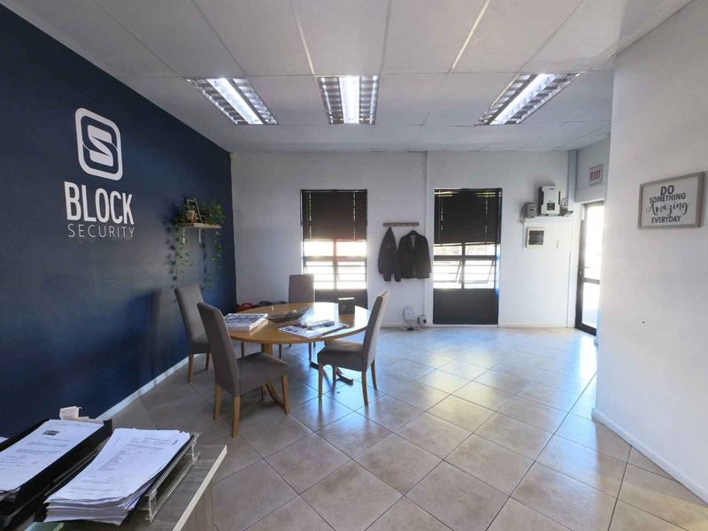 A functional office space featuring ceramic tiled flooring, a suspended ceiling with recessed lighting, and large windows with security gates.