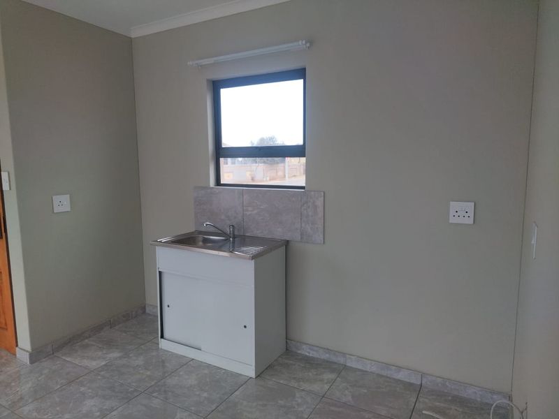 A compact, empty kitchen area featuring tiled flooring, a stainless steel sink with a tiled splashback, and neutral wall finishes.