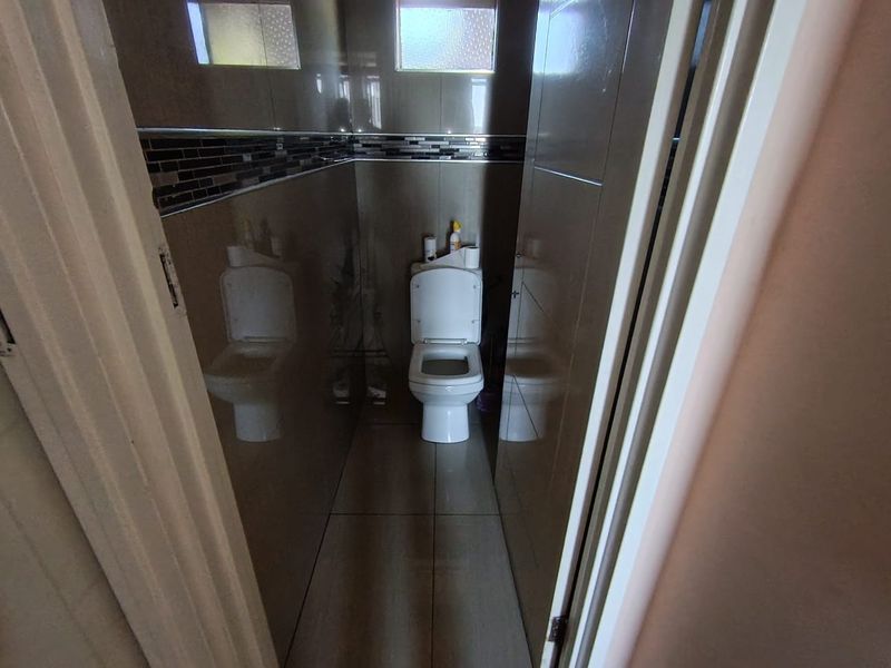 A compact, tiled bathroom featuring a standard toilet and high-set frosted glass windows for privacy.