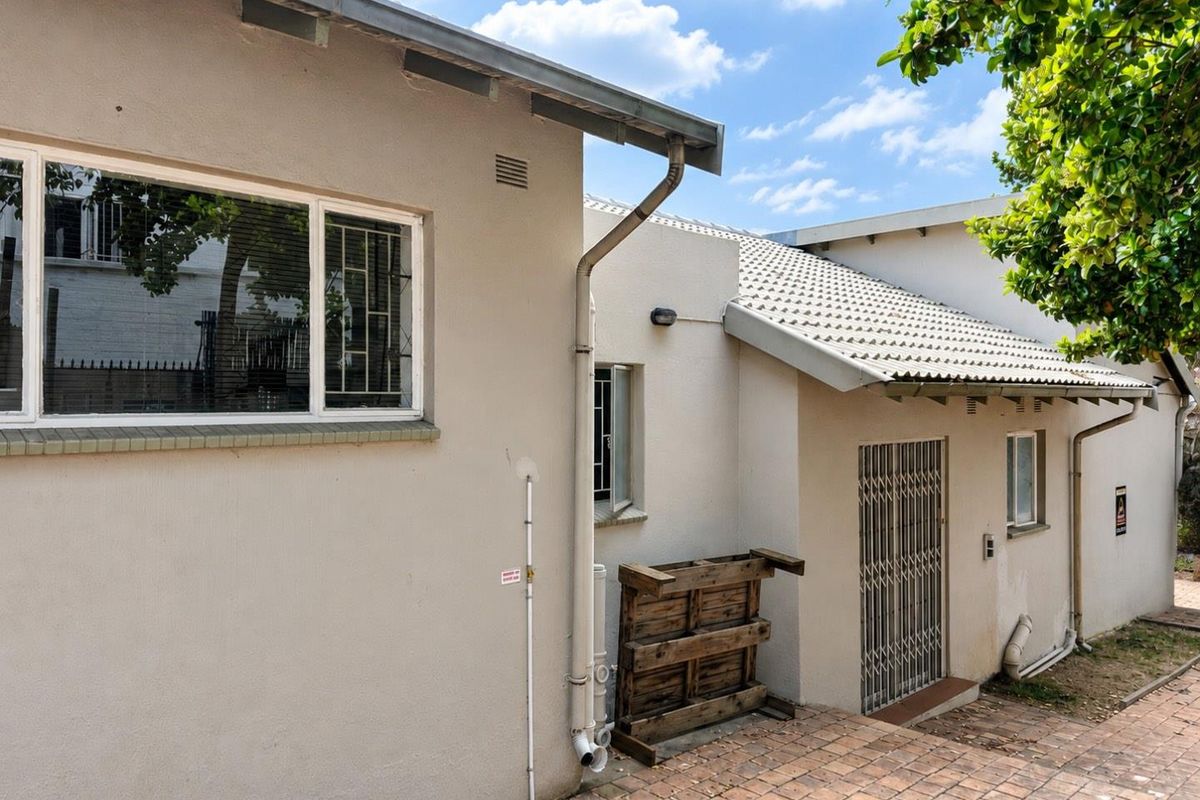 Rear exterior view of the apartment building featuring a paved walkway, security gate, and tiled roof structure.