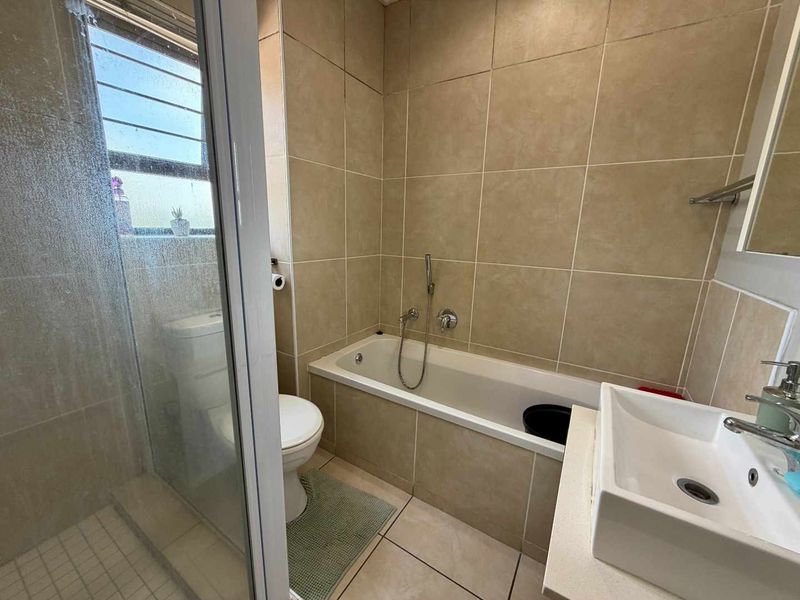 A functional bathroom featuring a tiled shower enclosure, a built-in bathtub, a modern basin, and a toilet with neutral wall tiling.