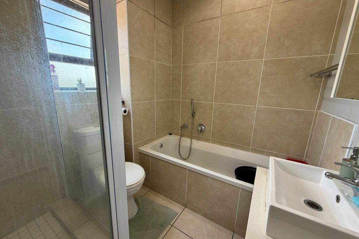 A functional bathroom featuring a tiled shower enclosure, a built-in bathtub, a modern basin, and a toilet with neutral wall tiling.