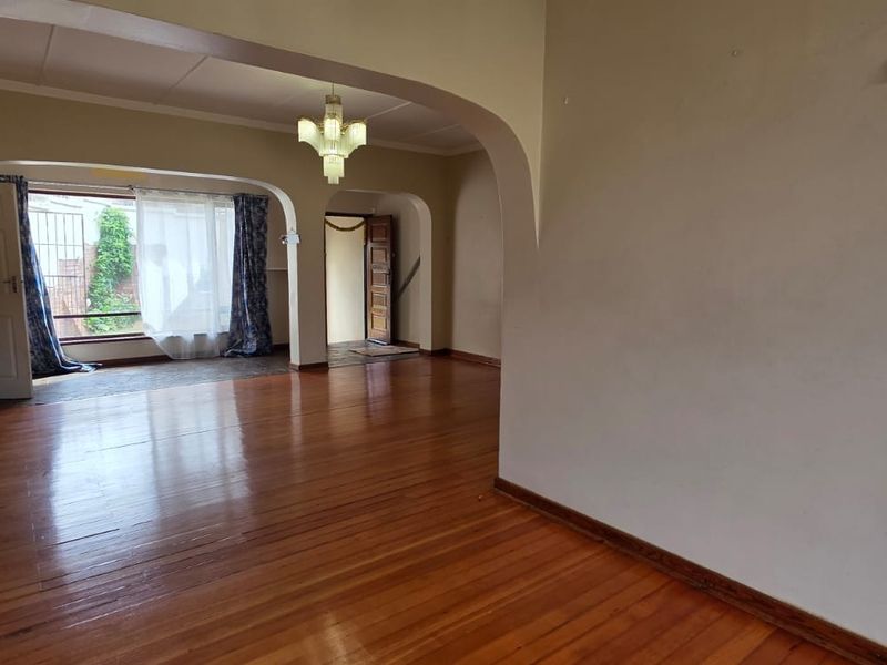 Spacious living area featuring polished hardwood flooring, classic architectural archways, and a central chandelier, offering a bright and open layout.