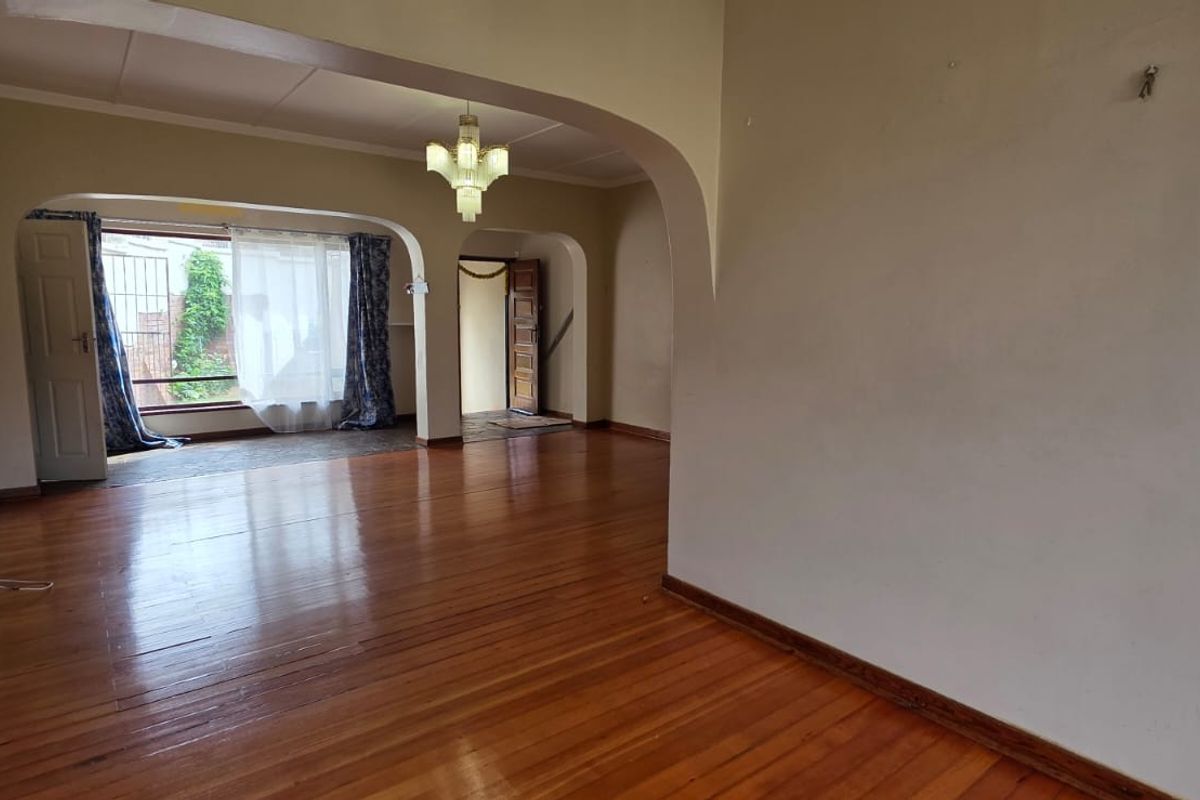 Spacious living area featuring polished hardwood flooring, classic architectural archways, and a central chandelier, offering a bright and open layout.