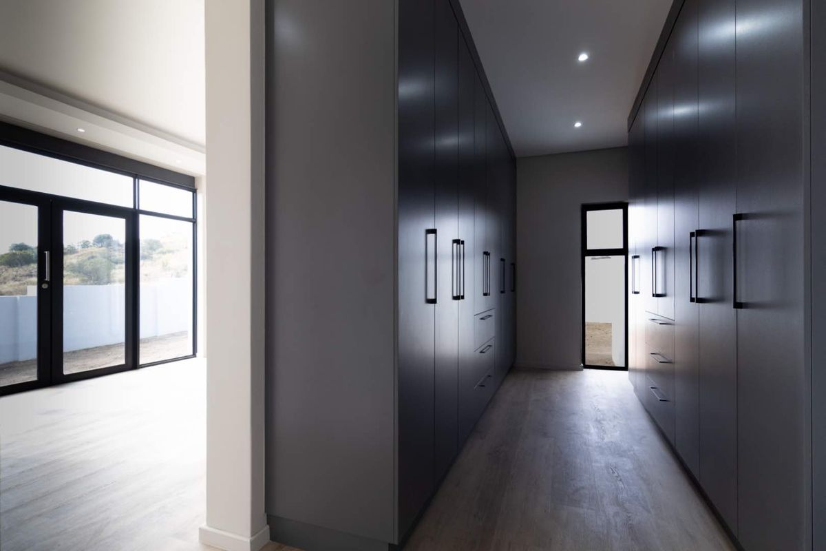 A modern walk-in dressing area featuring extensive floor-to-ceiling dark cabinetry, recessed lighting, and light wood-look flooring.