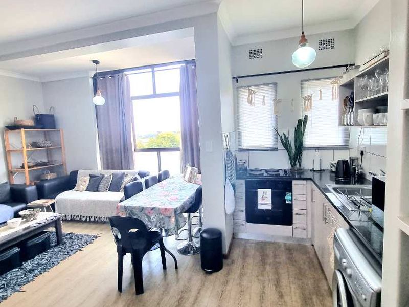 Open-plan living and kitchen area featuring modern laminate flooring, sleek cabinetry, granite countertops, and integrated appliances, creating a functional and bright living space.