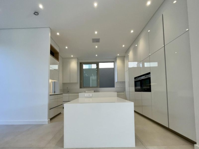 Modern kitchen featuring high-gloss white cabinetry, a central island, integrated double ovens, and recessed ceiling lighting.