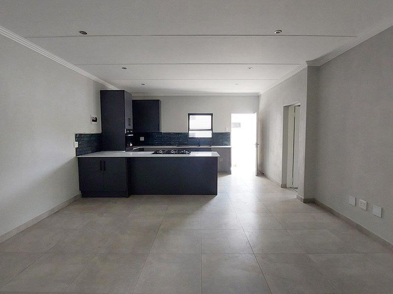 An open-plan living and kitchen area featuring modern dark cabinetry, a gas hob, tiled flooring, and recessed lighting in a neutral, well-maintained space.