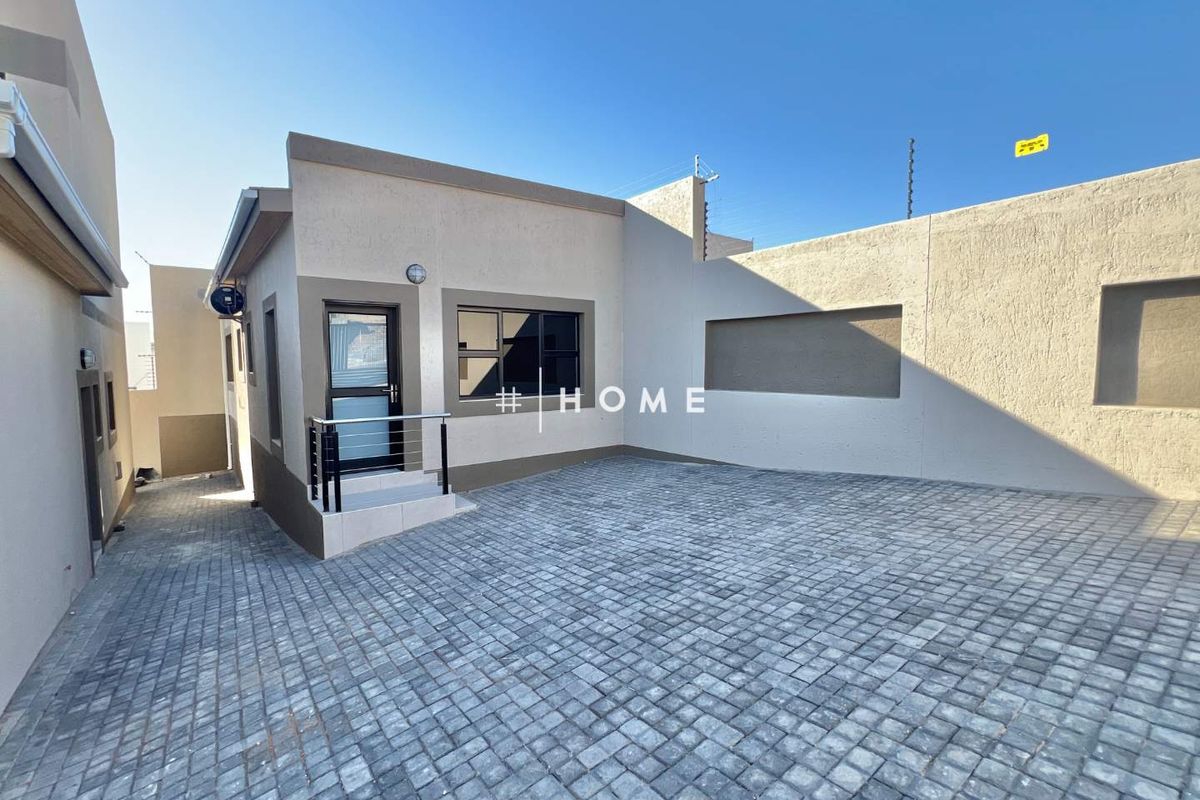 A well-maintained rear exterior area featuring a paved courtyard, secure boundary walls with electric fencing, and modern aluminium window frames.
