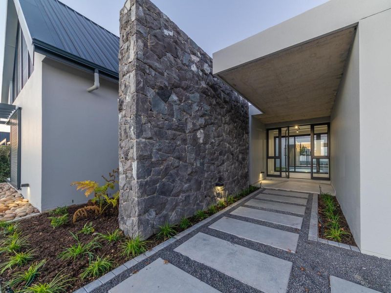 Modern front entrance featuring a striking stone feature wall, concrete canopy, and a paved walkway leading to a glass-panelled front door.