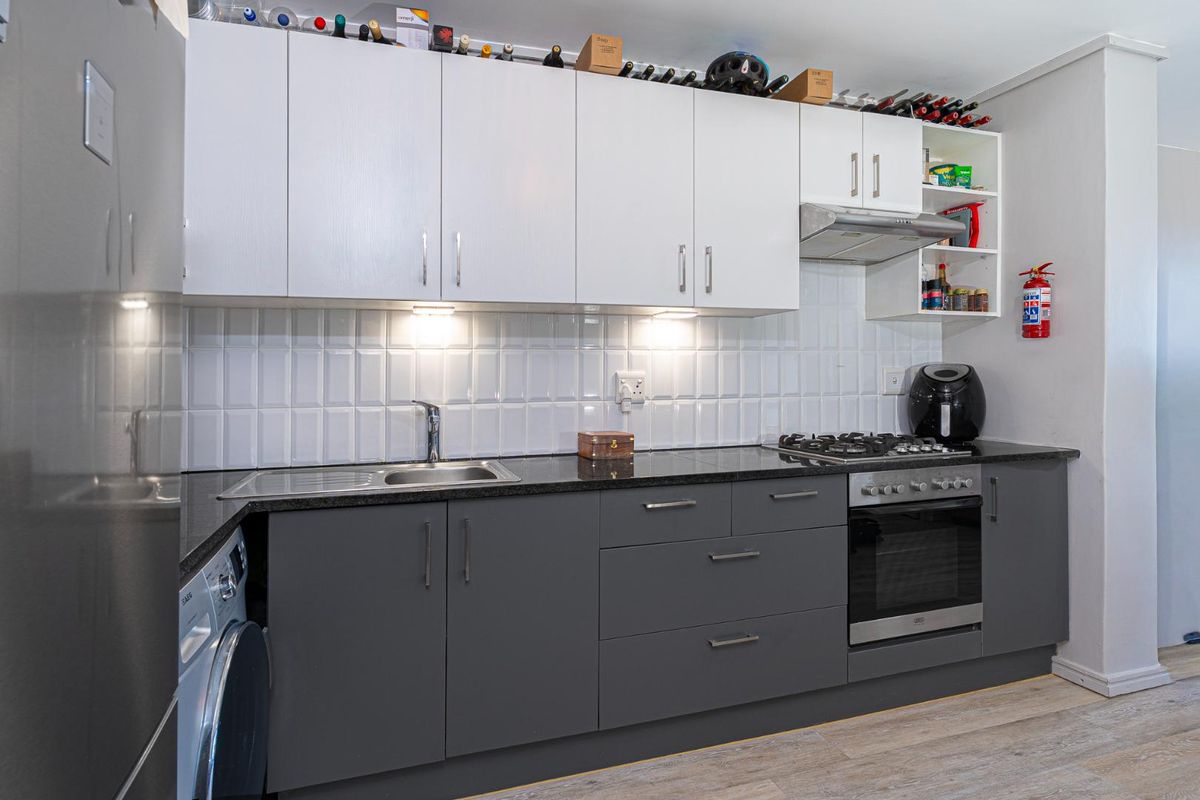 Modern kitchen featuring dark grey lower cabinetry, white upper cabinets, granite countertops, subway tile backsplash, and integrated stainless steel oven and gas hob.