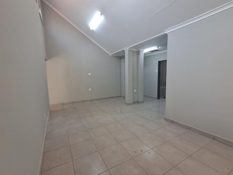 An empty, open-plan living area featuring vaulted ceilings, tiled flooring, and neutral wall finishes, offering a blank canvas for interior design.