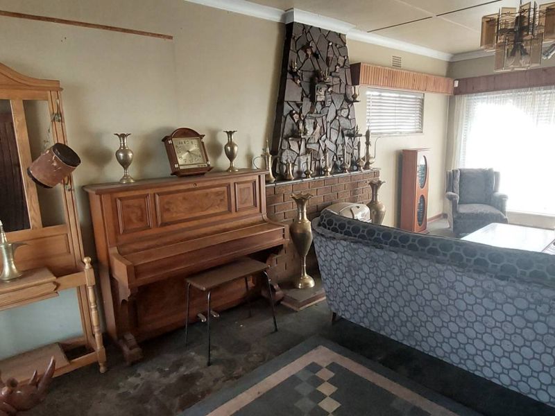 Spacious living room featuring a prominent stone-clad fireplace, tiled flooring, and a ceiling fan, offering a dated interior ready for modernization.