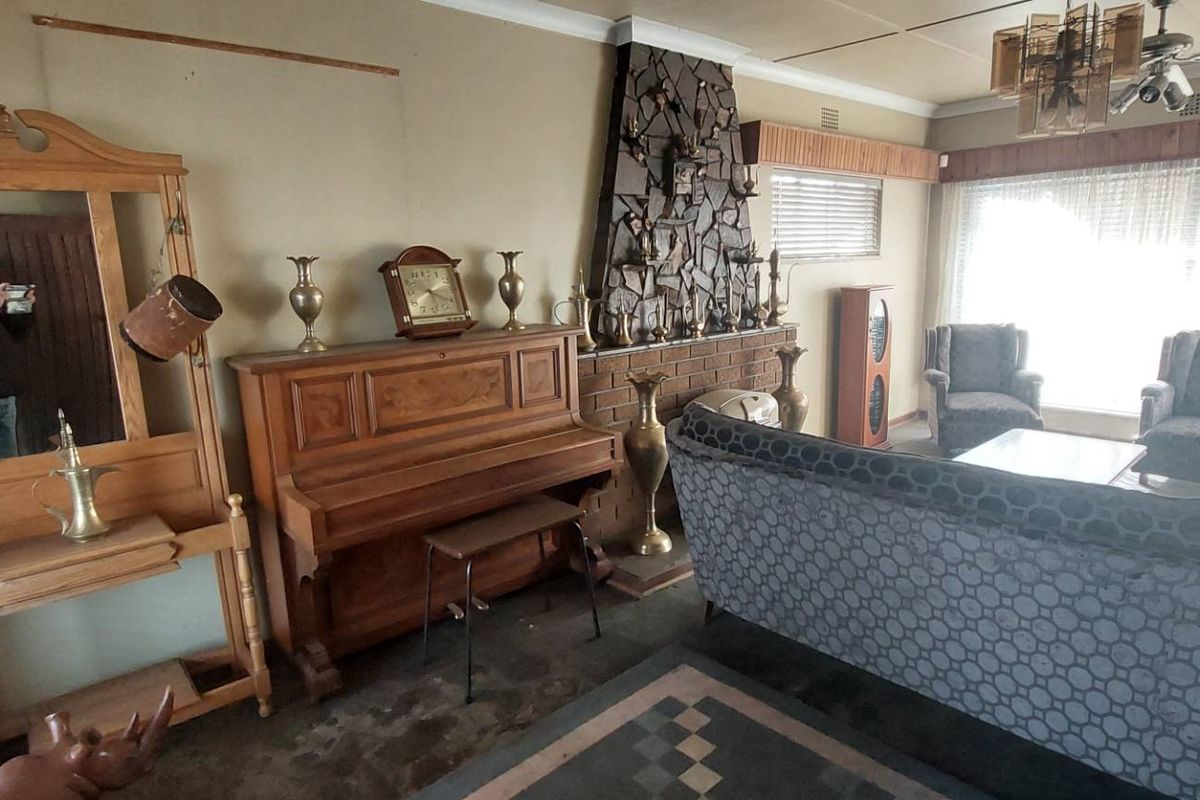 Spacious living room featuring a prominent stone-clad fireplace, tiled flooring, and a ceiling fan, offering a dated interior ready for modernization.