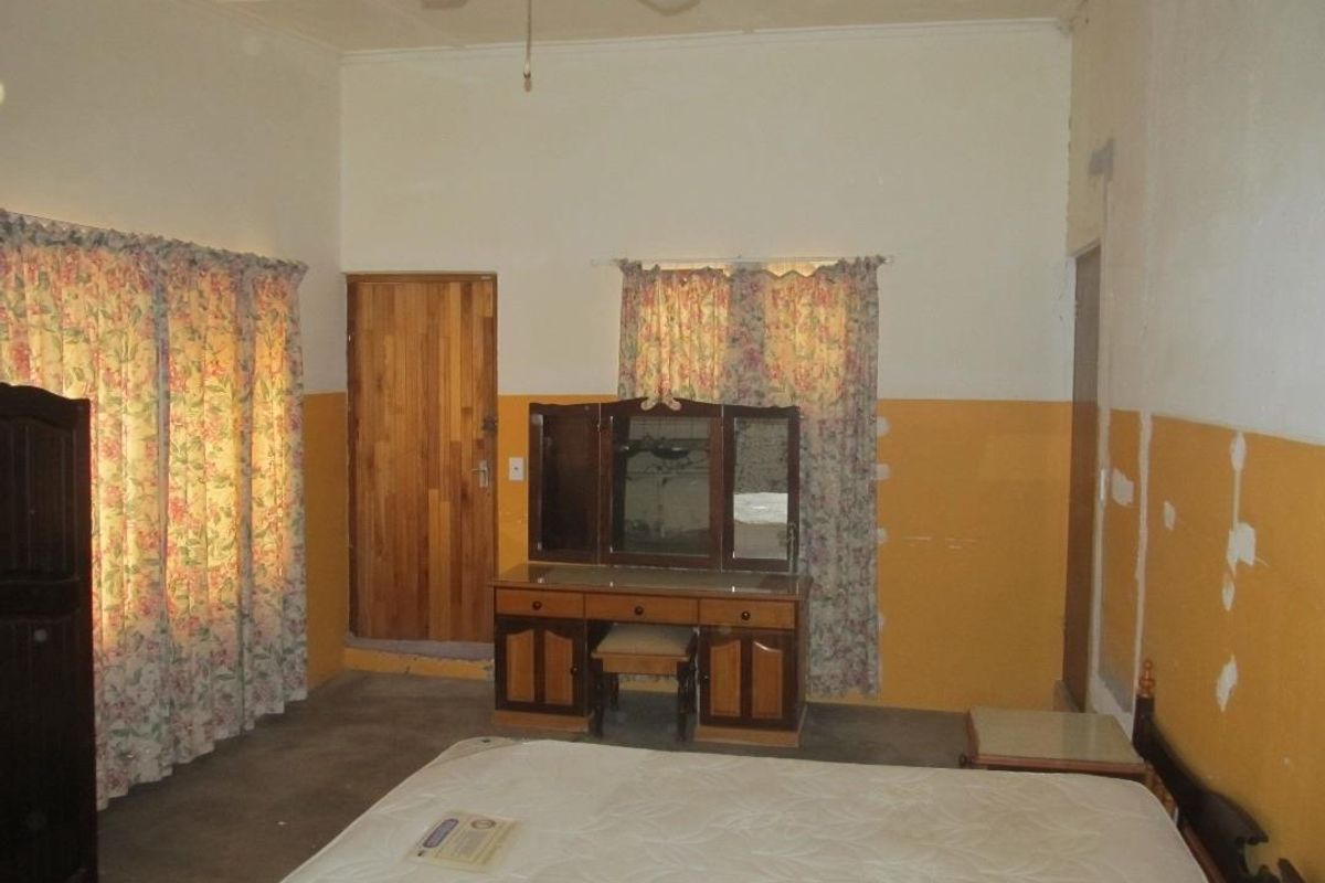 A bedroom featuring a ceiling fan, wooden door, and windows with curtains, requiring cosmetic updates to the wall finishes and flooring.