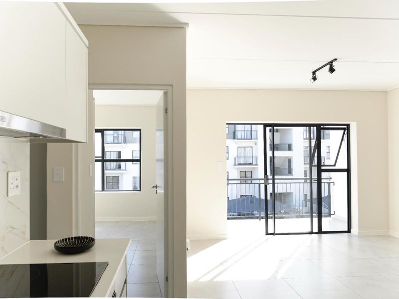 Modern open-plan apartment featuring a sleek kitchen with built-in hob, tiled flooring, and a bright living area leading to a private balcony.
