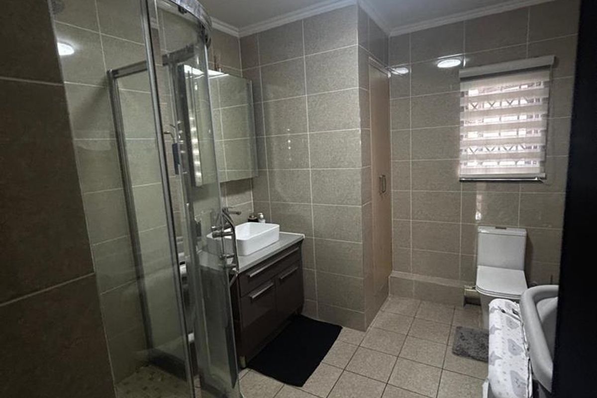 A functional bathroom featuring a curved glass shower enclosure, a vanity with a vessel sink, a toilet, and neutral floor-to-ceiling wall tiling.