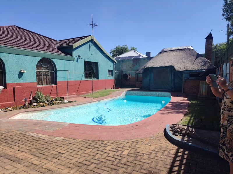 Outdoor pool area featuring a swimming pool, paved surround, and a traditional thatched lapa structure in the rear garden.
