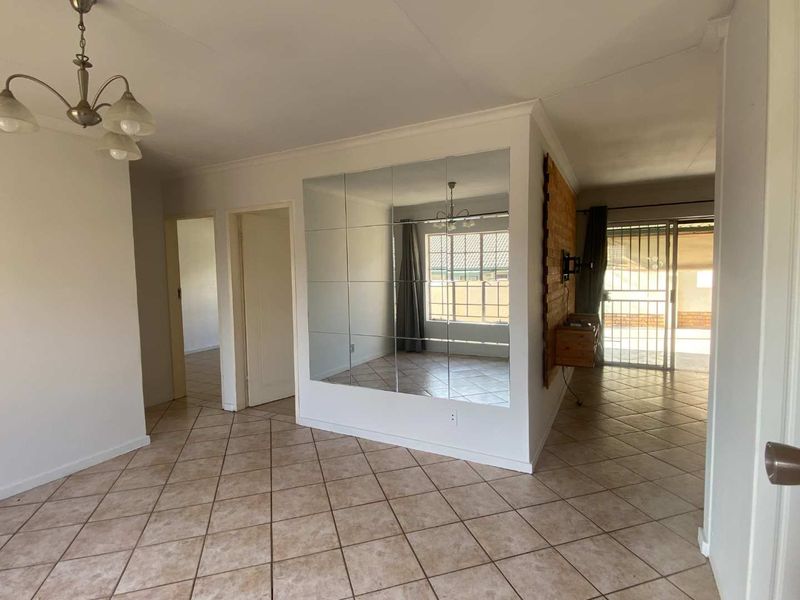 Spacious living area featuring tiled flooring, a large mirrored feature wall, and direct access to an outdoor patio through sliding glass doors.