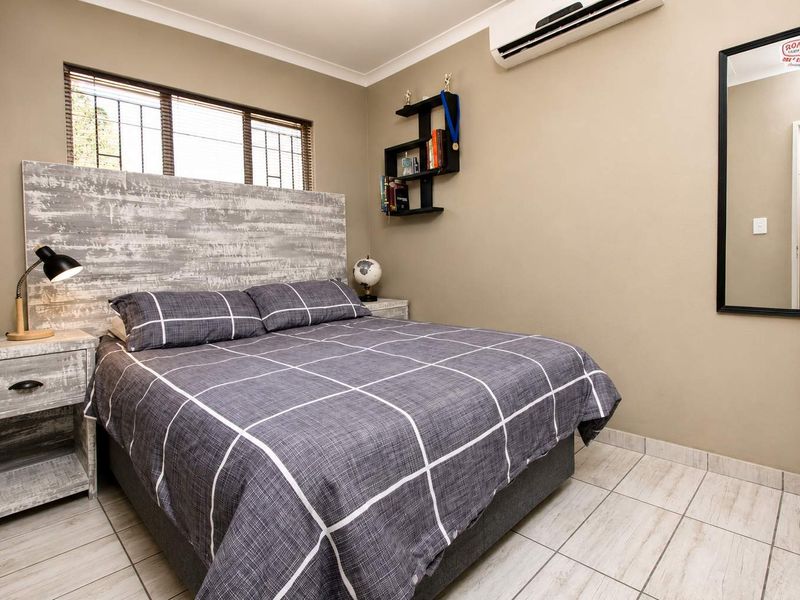A well-maintained bedroom featuring tiled flooring, a wall-mounted split-system air conditioner, and security bars on the window.