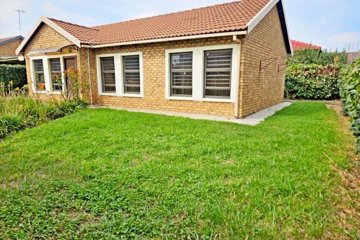 Rear view of a face brick house featuring a tiled roof, aluminium window frames, and a surrounding lawn area.