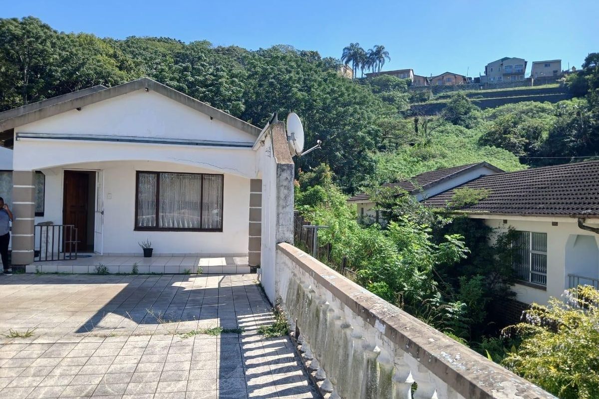 Rear exterior view showing a tiled patio area with a concrete balustrade, adjacent to the main house structure with visible weathering.