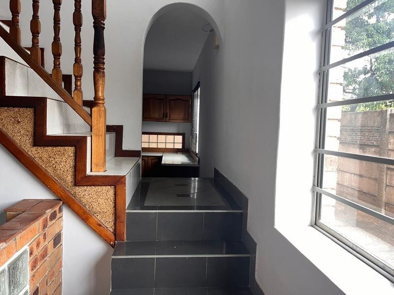 A transition hallway featuring a timber staircase, tiled steps, and an arched entryway leading to a kitchen area with built-in cabinetry.