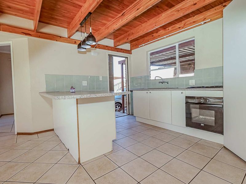 Functional kitchen featuring exposed timber ceiling beams, tiled flooring, built-in oven, hob, and a central island with a tiled backsplash.
