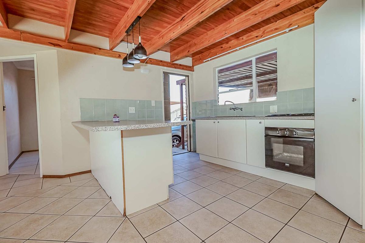 Functional kitchen featuring exposed timber ceiling beams, tiled flooring, built-in oven, hob, and a central island with a tiled backsplash.